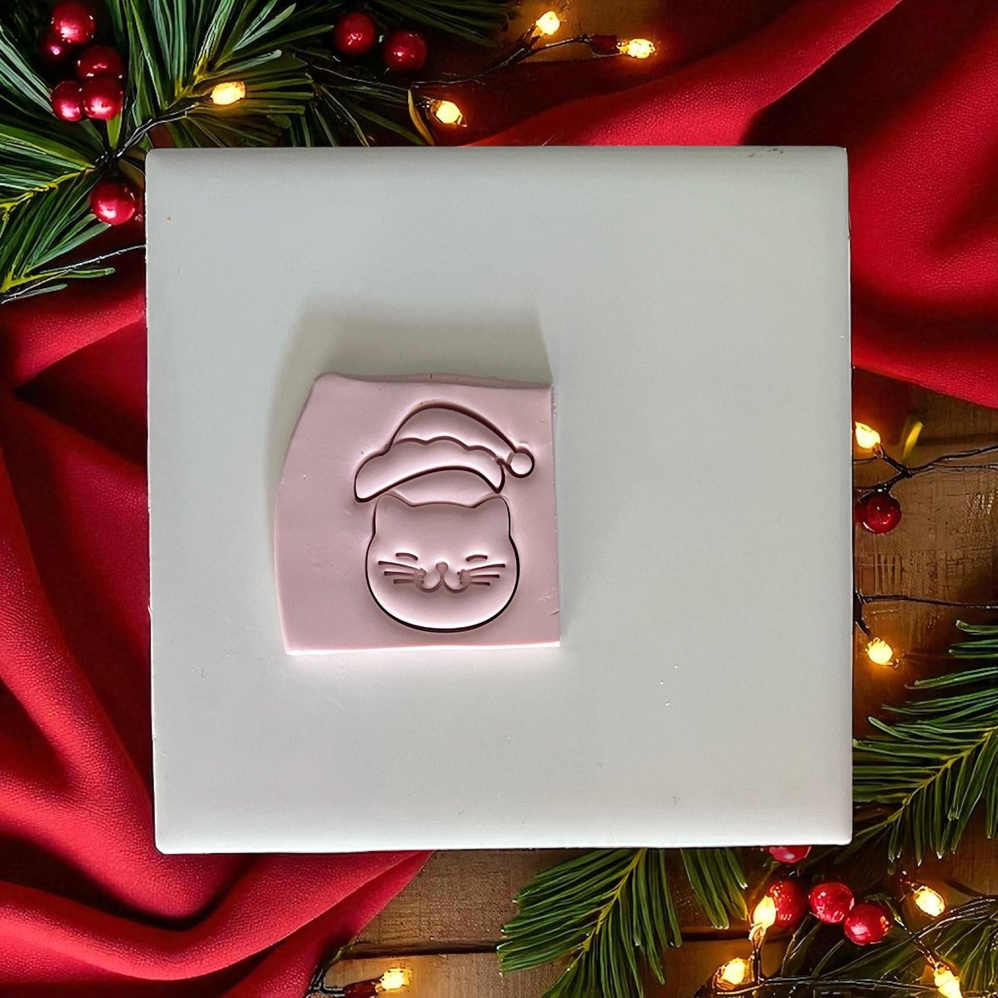 Santa kitty clay imprint on pink clay slab with lights and greenery