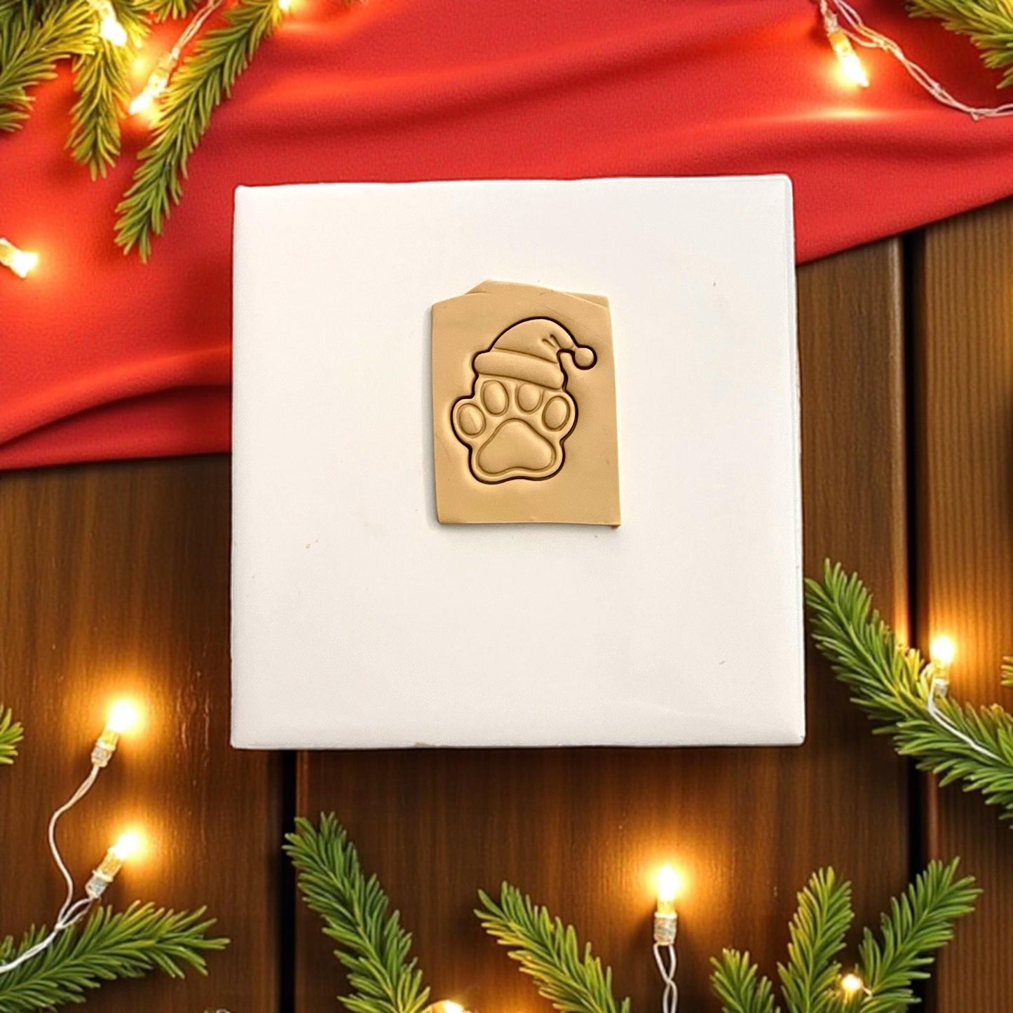 Christmas paw print polymer clay imprint with Santa hat on tan clay with festive lights