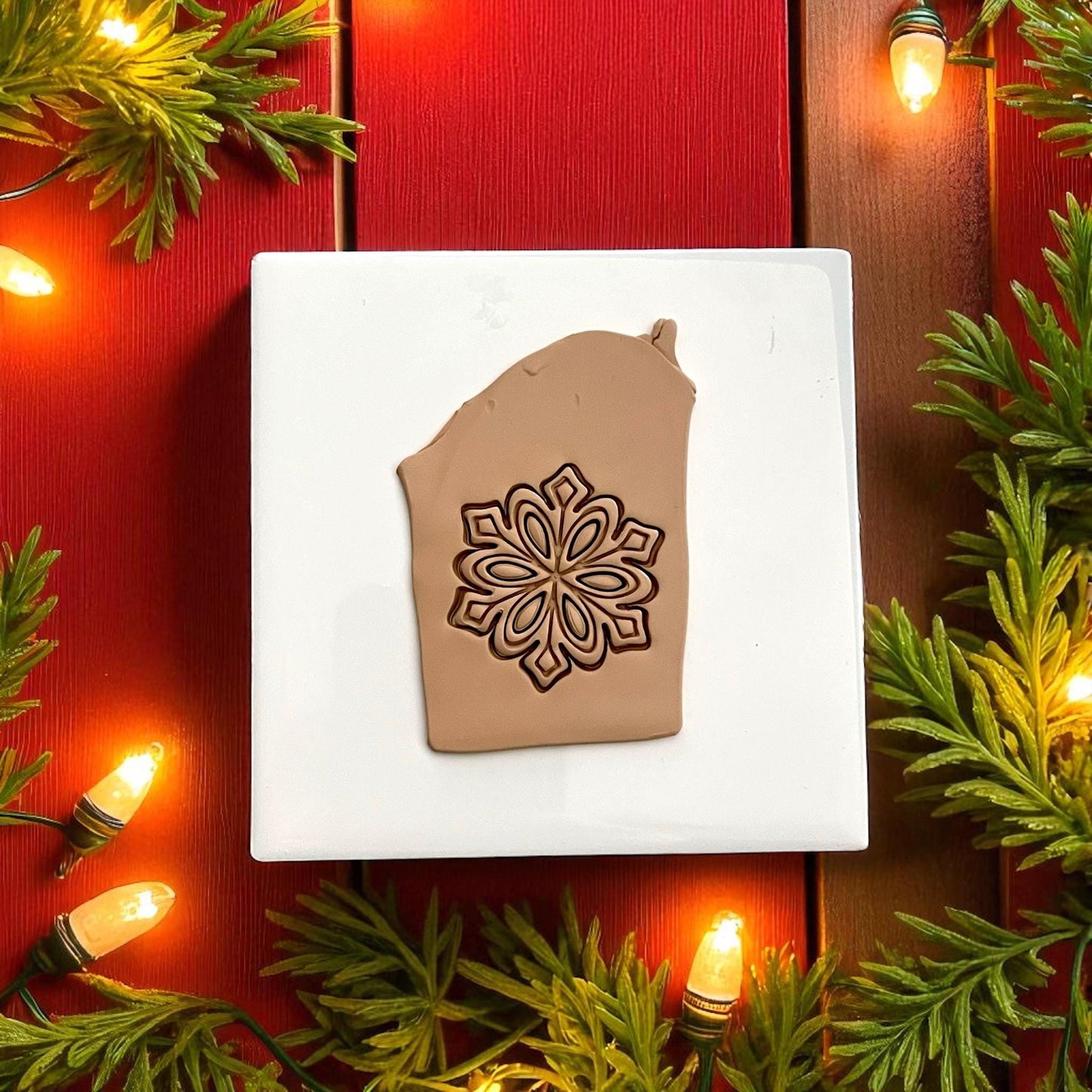 Snowflake polymer clay imprint on tan clay with red background and holiday lights