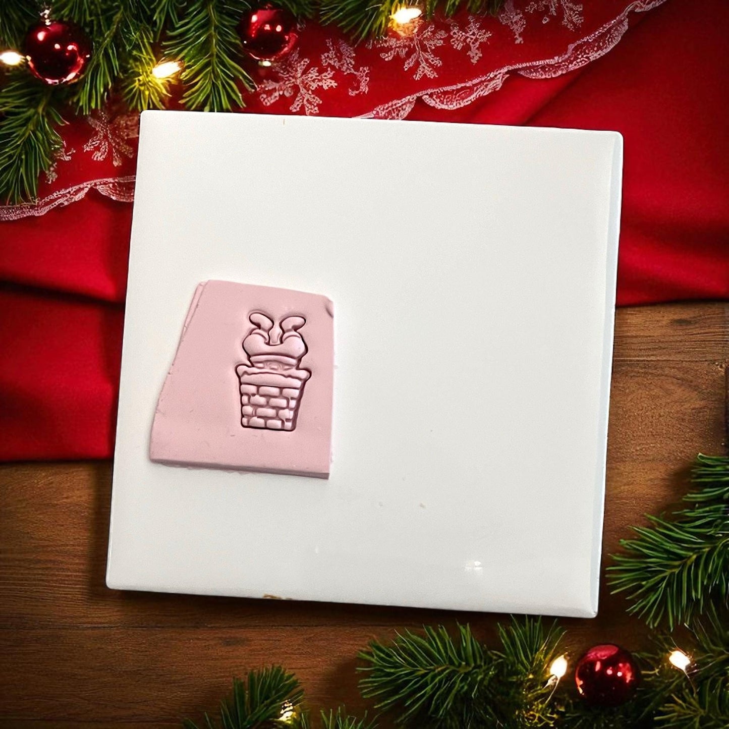Pink clay imprint of Santa stuck in chimney polymer clay cutter on white tile with red cloth
