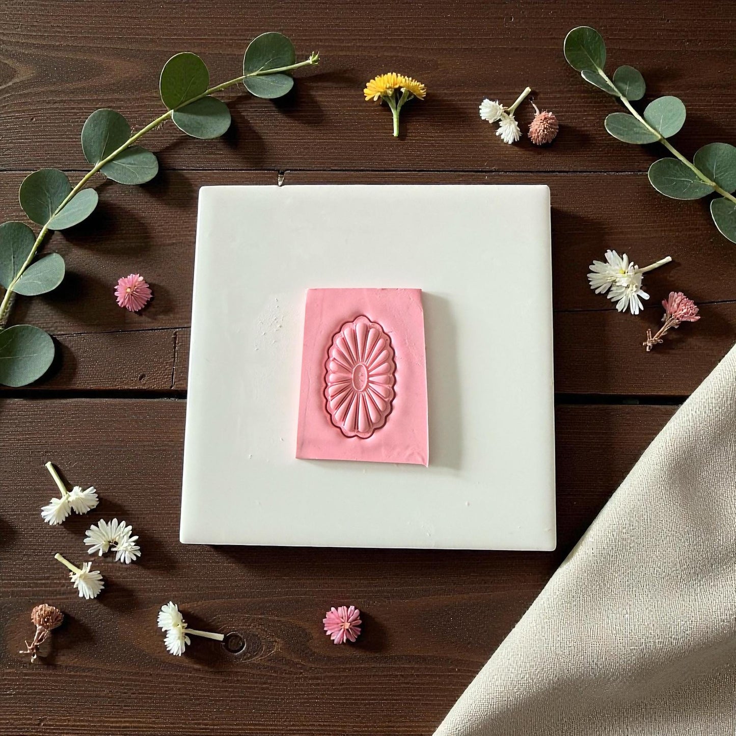 Pink oval floral polymer clay cutter on brown wood with beige fabric and eucalyptus branch