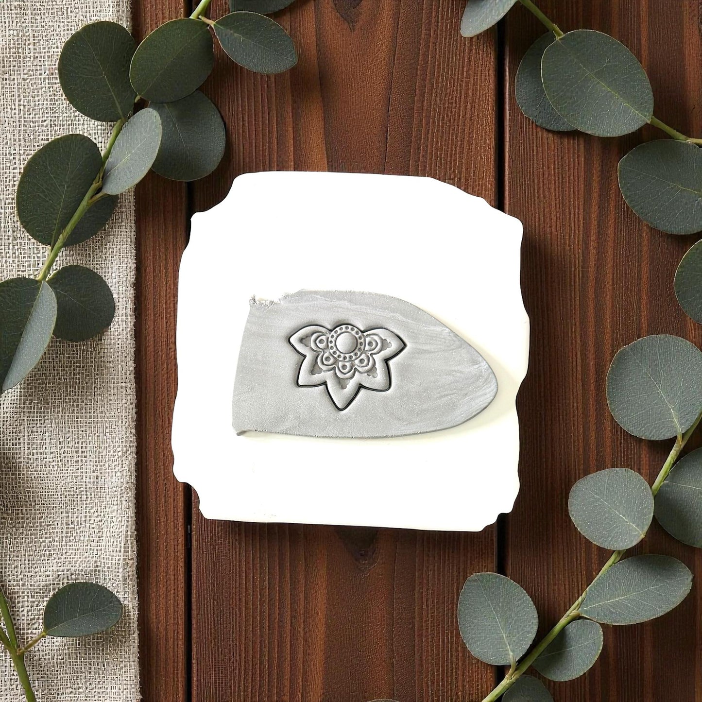 Gray boho flower imprint on clay slab surrounded by eucalyptus