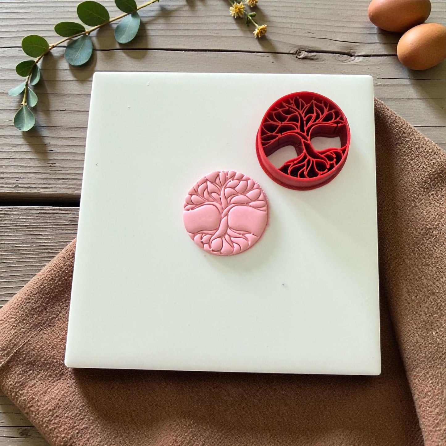 Clay impression of tree of life design next to red cutter on fabric background