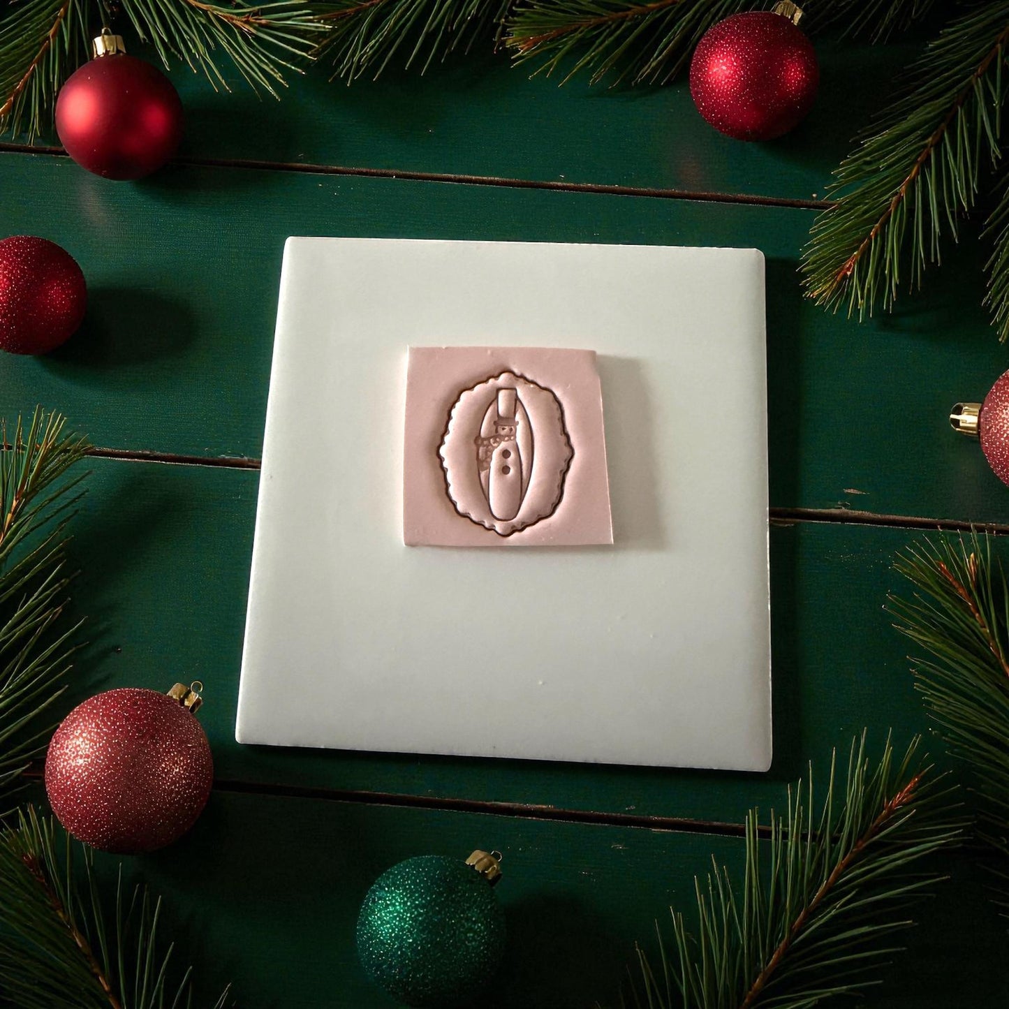 Pink snowman cameo clay imprint centered on white tile with green and red ornaments
