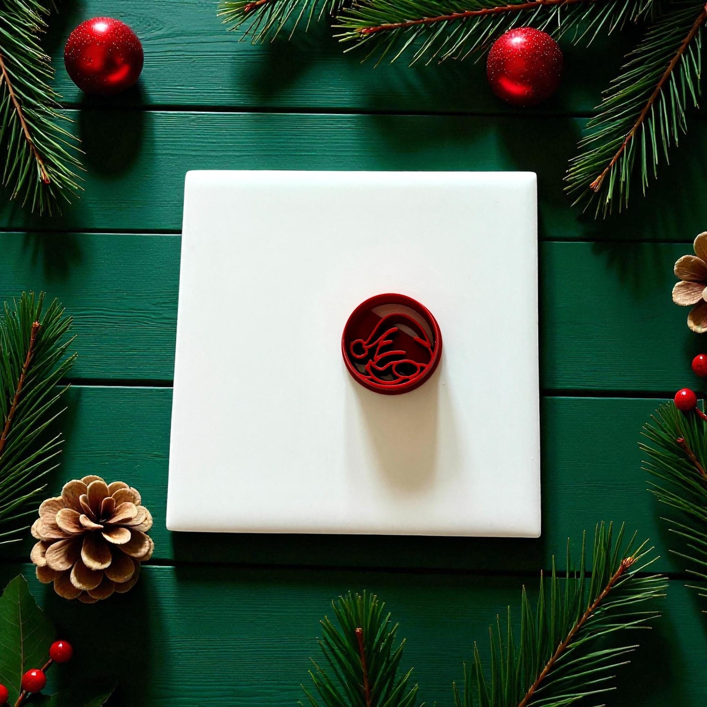 Red gnome cutter centered on white tile with holiday greenery and pinecones
