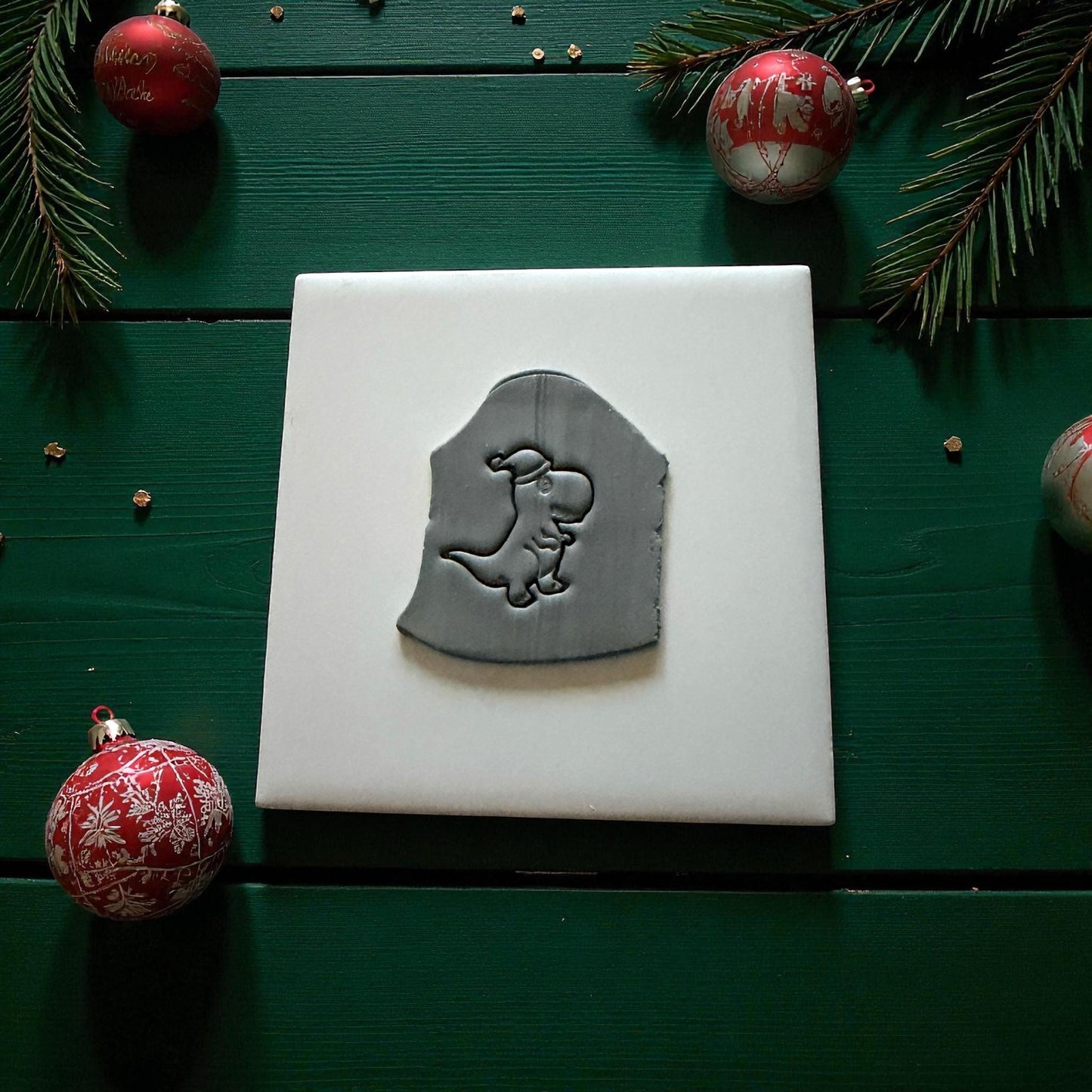 Gray dinosaur clay imprint on white tile with Christmas ornaments and pine branches