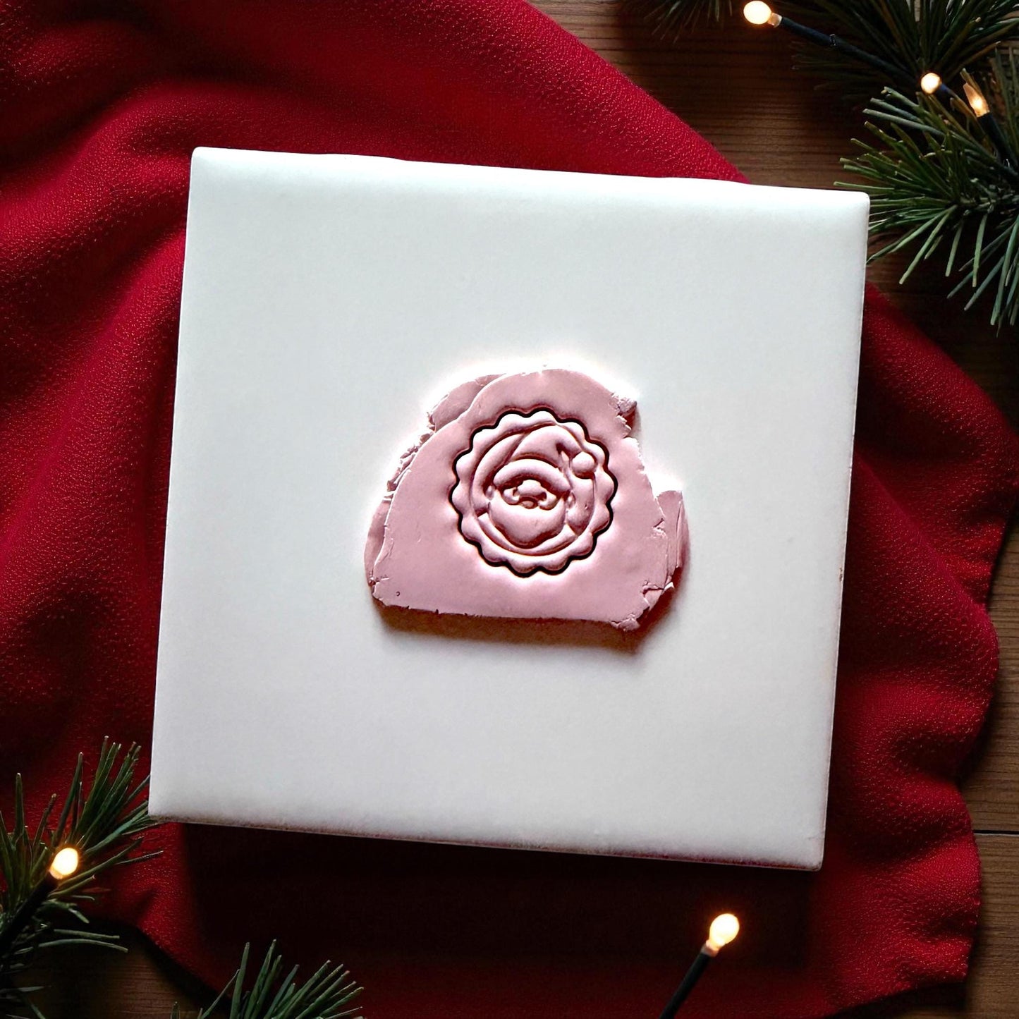 Pink Santa imprint on white tile with red fabric and pine sprigs
