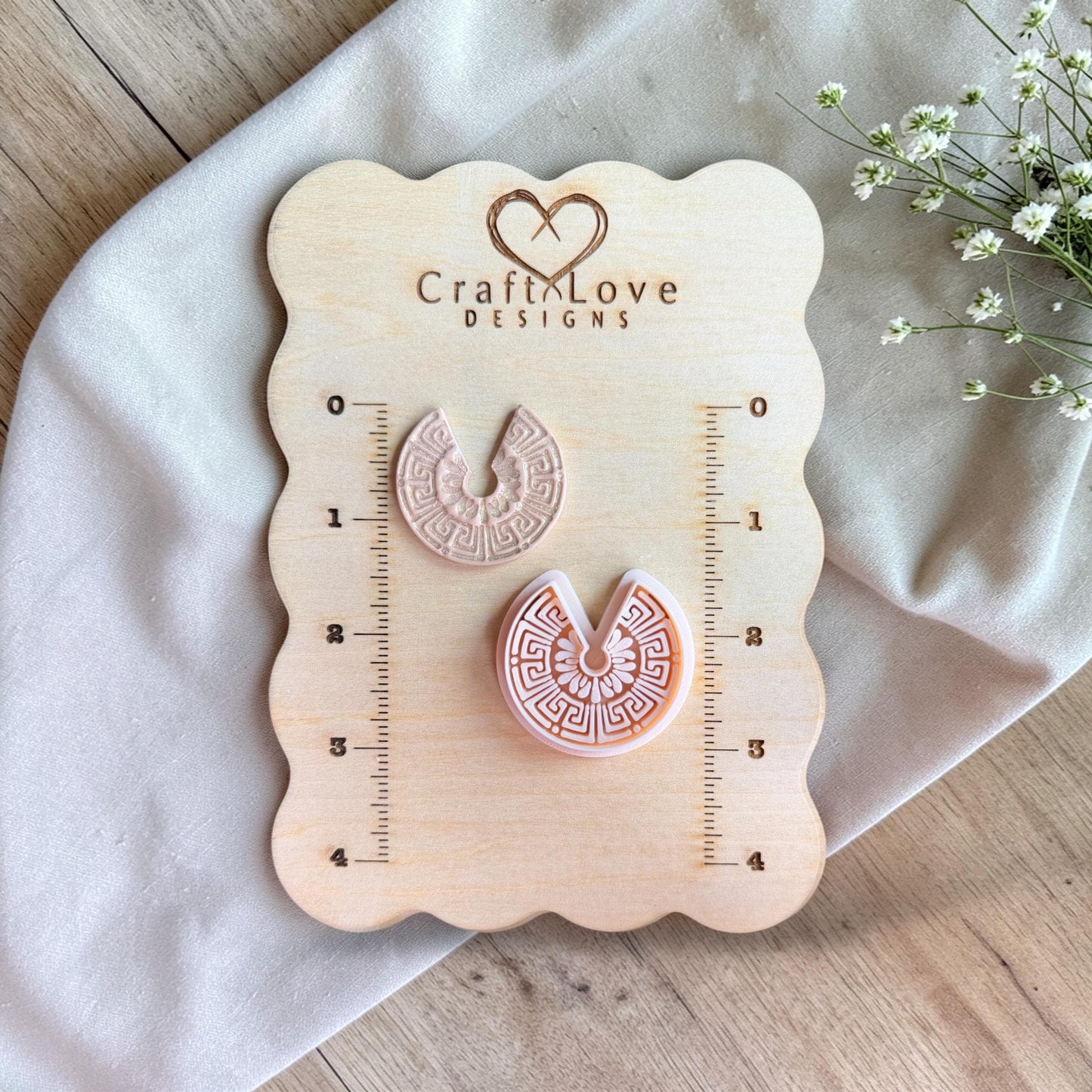 Cutter and finished clay piece displayed on a wooden measuring board with ruler markings and soft floral accents.