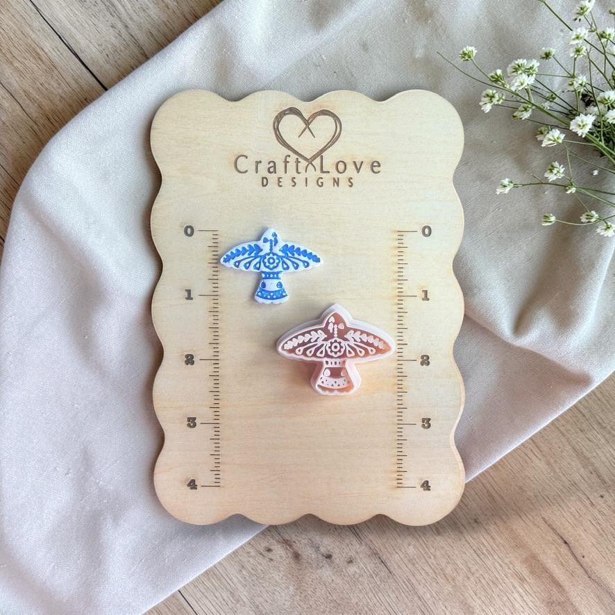 Polymer clay cutter with detailed folk art bird design displayed on a wooden measuring board with ruler markings.