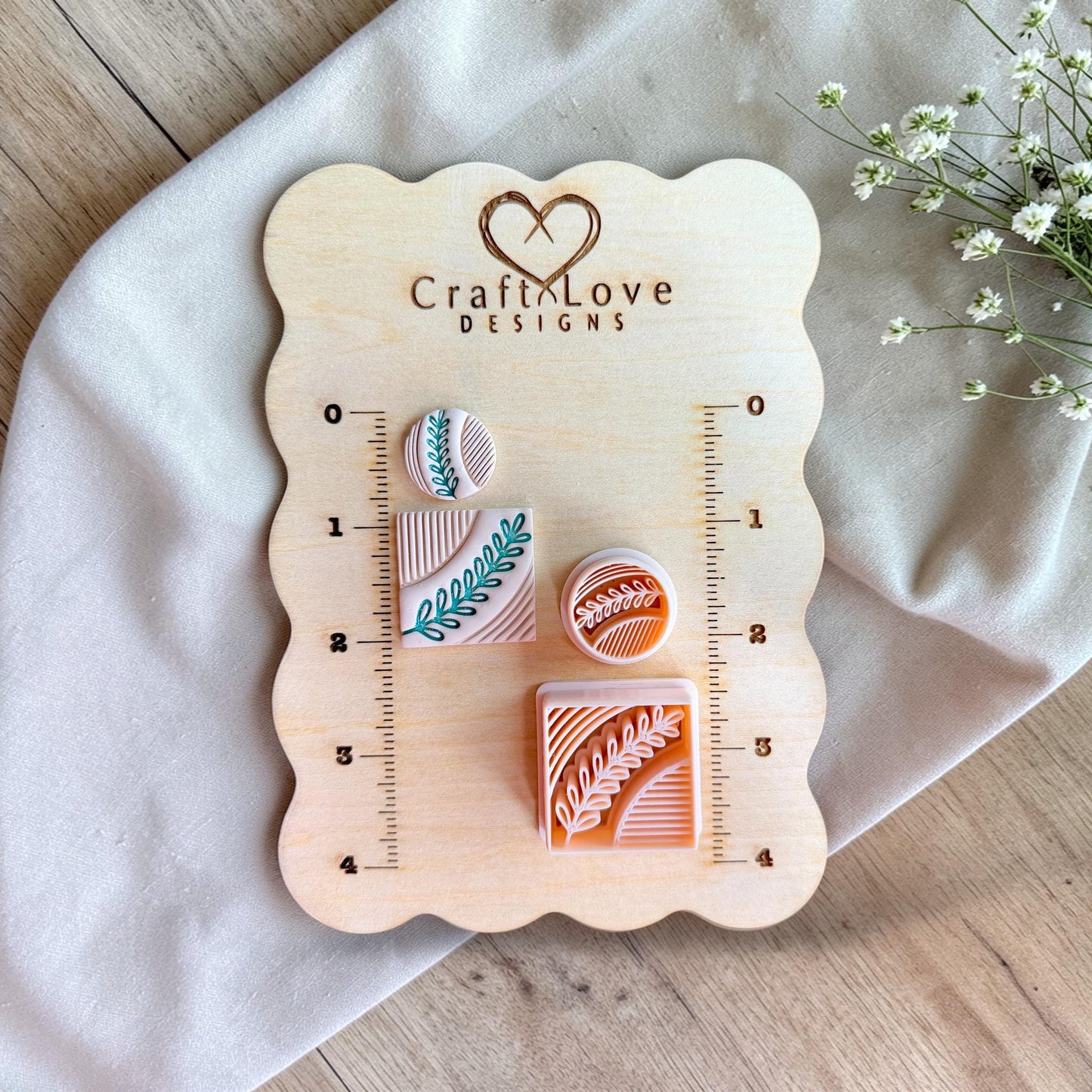 Square and circle polymer clay cutters with botanical leaf pattern displayed on a wooden measuring board with ruler markings.