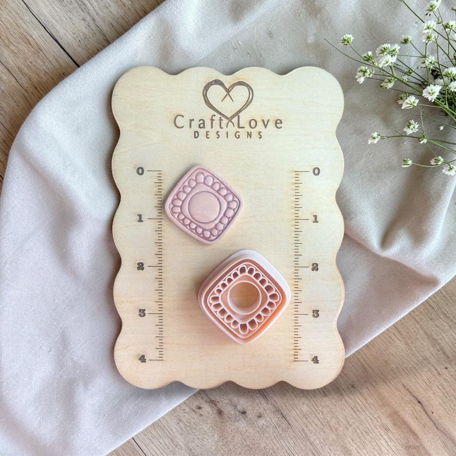 Cutter and finished clay piece displayed on a wooden measuring board with ruler markings and brand logo.