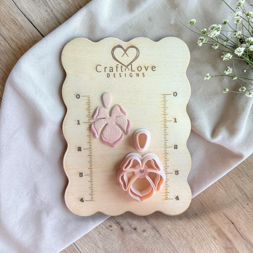 Polymer clay cutter set with tropical flower shape and matching top piece displayed on a wooden measuring board with ruler markings.