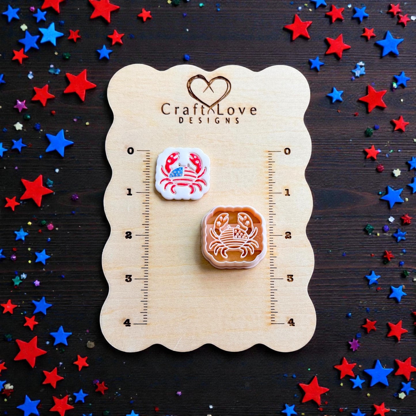 Patriotic crab polymer clay cutter and finished red white and blue crab clay piece displayed on CraftLove Designs measurement board with star confetti