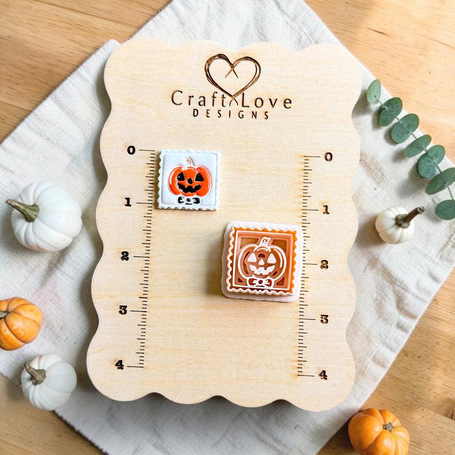 Framed jack-o-lantern pumpkin clay piece and matching polymer clay cutter displayed on a measurement board with autumn pumpkins nearby.