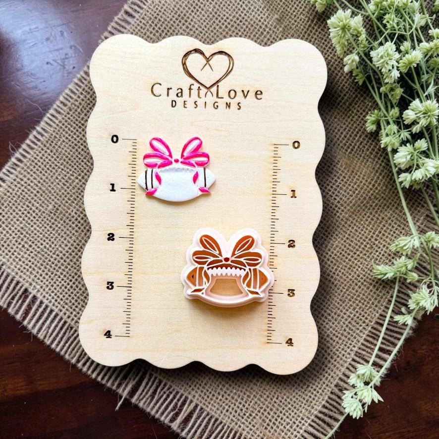 Finished coquette bow football clay piece beside the matching polymer clay cutter on a Craft Love Designs measurement board.
