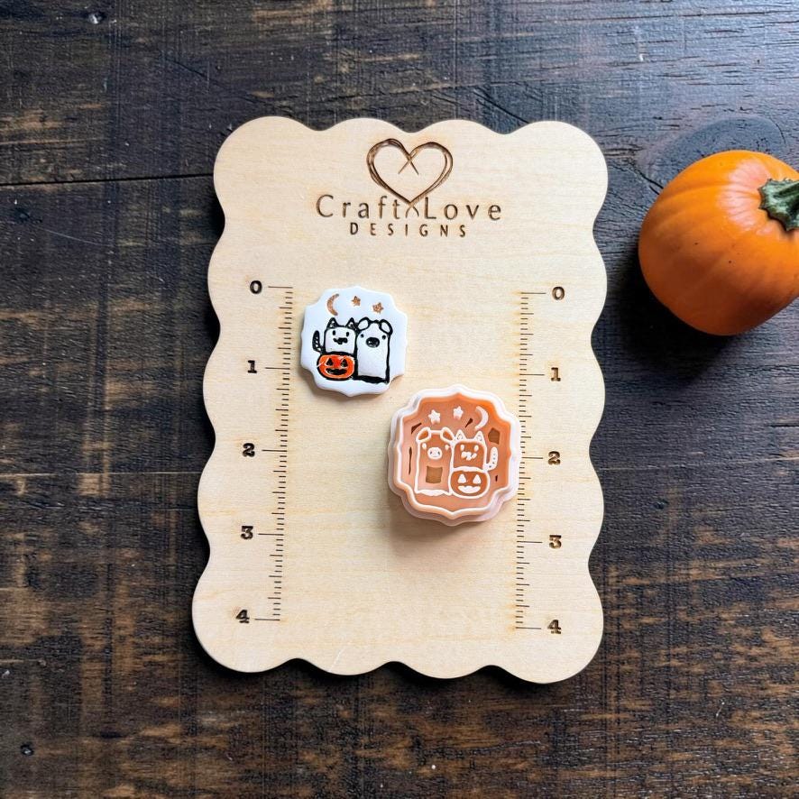 Halloween Pals finished clay piece and peach design displayed on a Craft Love Designs wooden measuring board, with ruler markings showing their scale and an orange pumpkin beside the board.