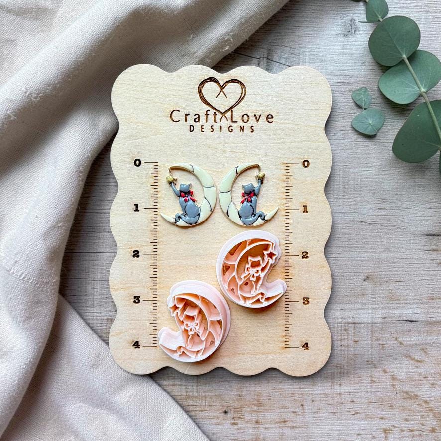 Two finished mirrored gray cat and crescent moon pieces displayed above their two matching separate designs on a Craft Love Designs wooden measurement board.