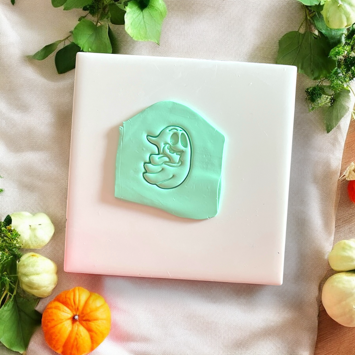 Silly Ghost cutter imprint on mint green clay slab surrounded by small pumpkins