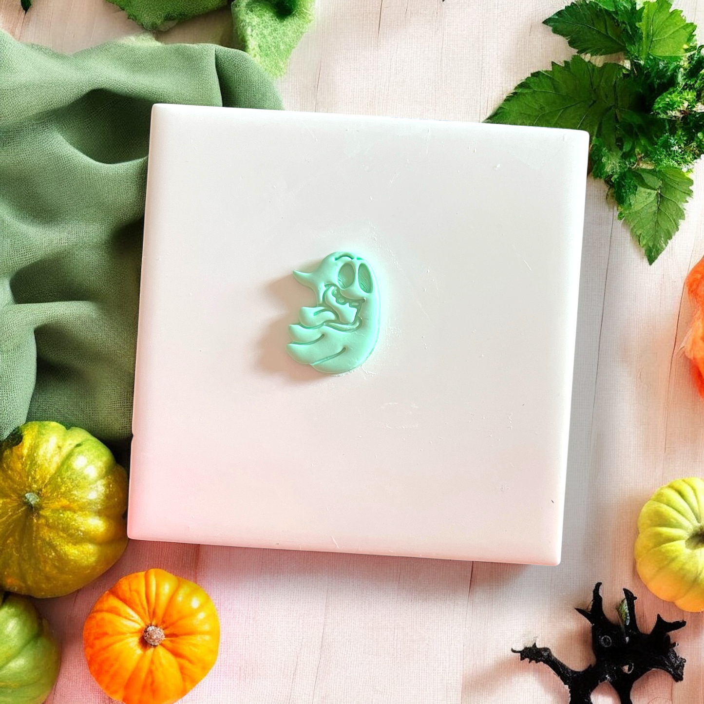 Silly Ghost clay cutout on white tile with fall decor and green fabric
