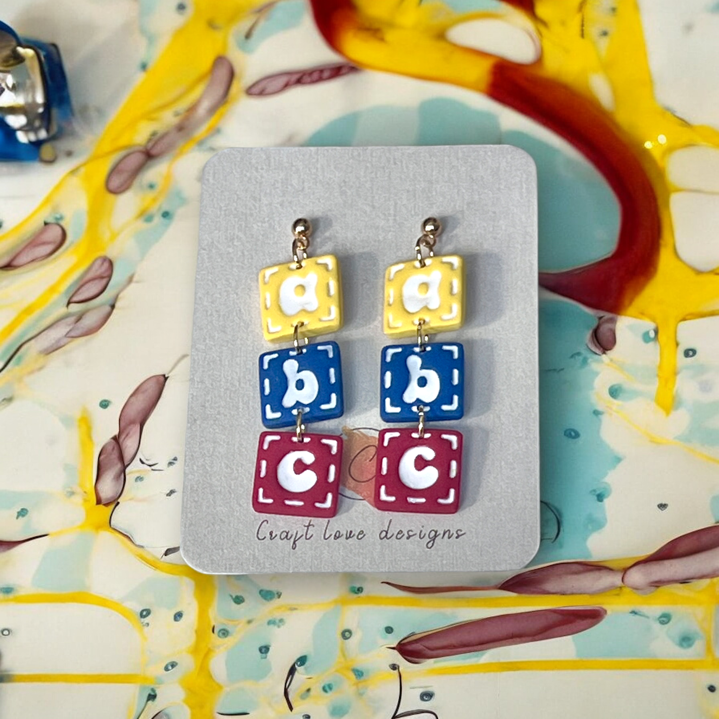 Colorful ABC block earrings displayed on a Craft Love Designs card, perfect for teachers or playful accessory lovers..