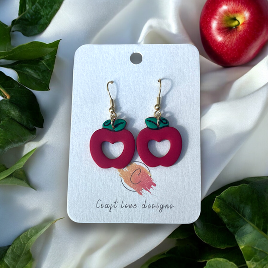 Red apple cutout earrings with green leaf accents displayed on a Craft Love Designs card, perfect for teachers or playful accessory lovers.