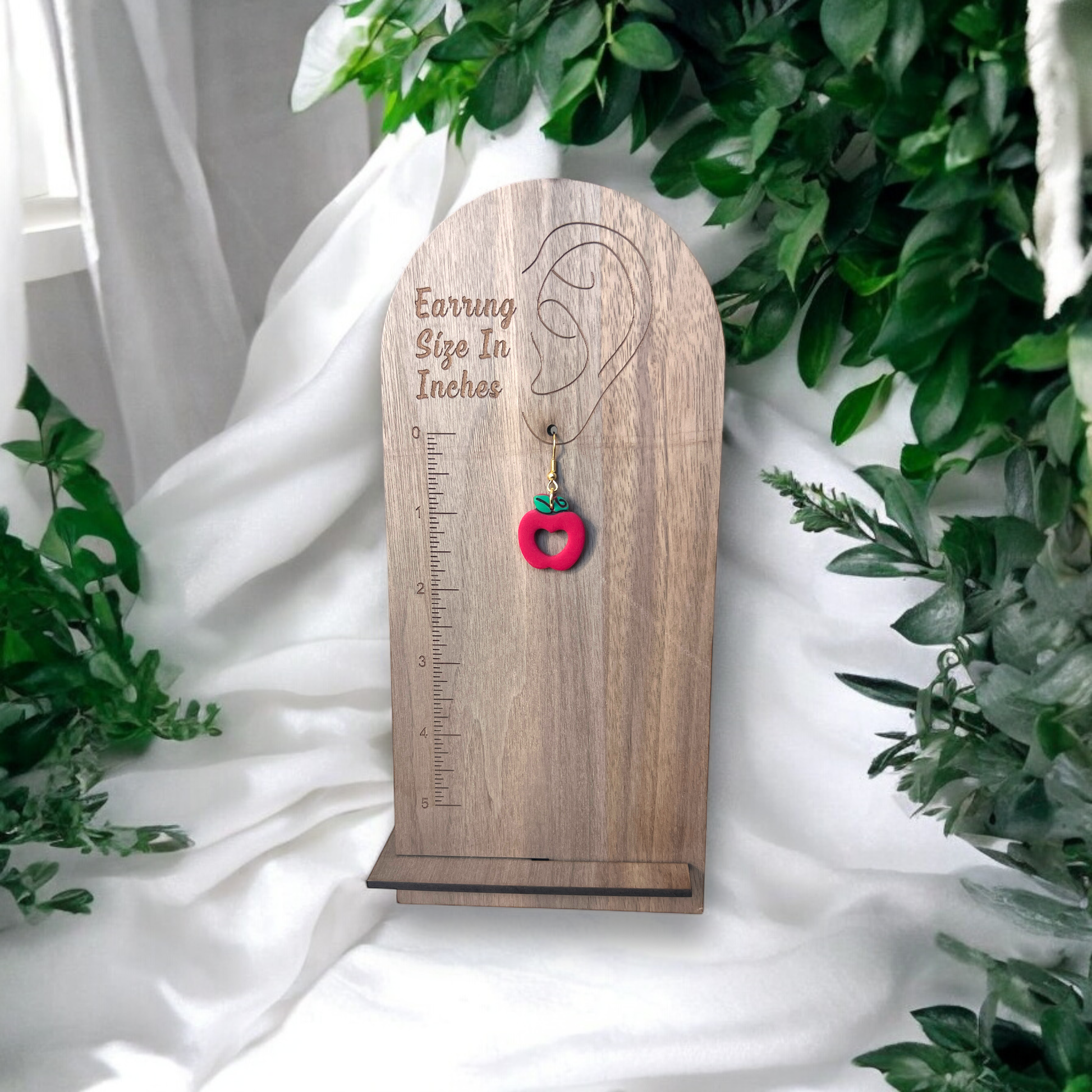 Red apple earrings with green leaf detail, displayed on a wooden earring size chart, showing their perfect length and fun design.