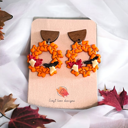 Orange wreath earrings displayed on a product card, decorated with fall leaves and acorns, evoking autumn vibes.
