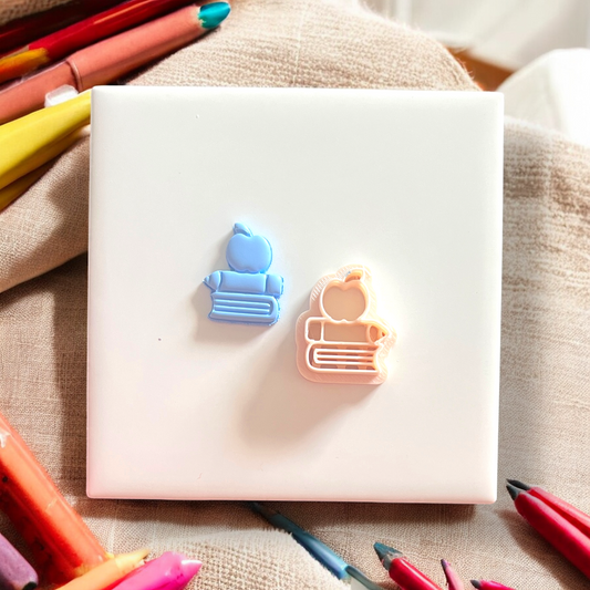 White square object with blue and pink bear-shaped clips on a beige fabric background with colorful markers.