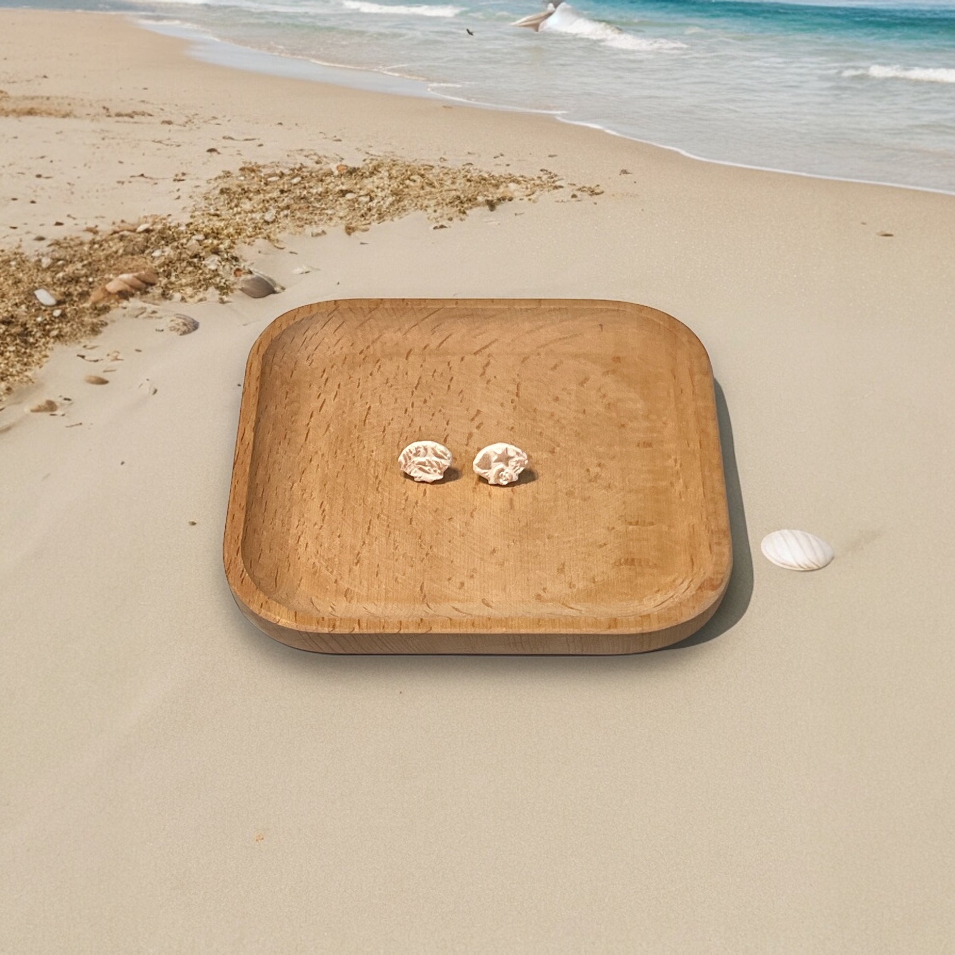 Small textured earrings displayed on a wooden plate by the beach, capturing a natural and serene beach vibe. 