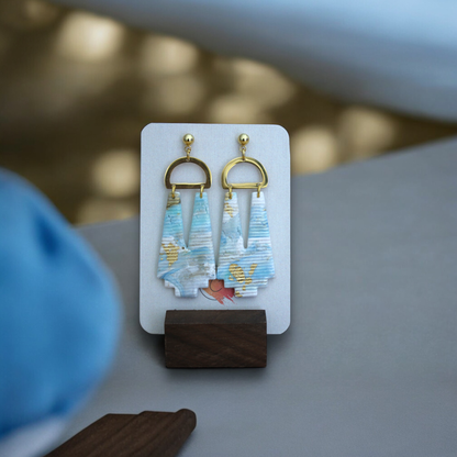 Beachy marbled earrings featuring blue, beige, and gold details, shown on a textured woven background for a natural, coastal vibe.