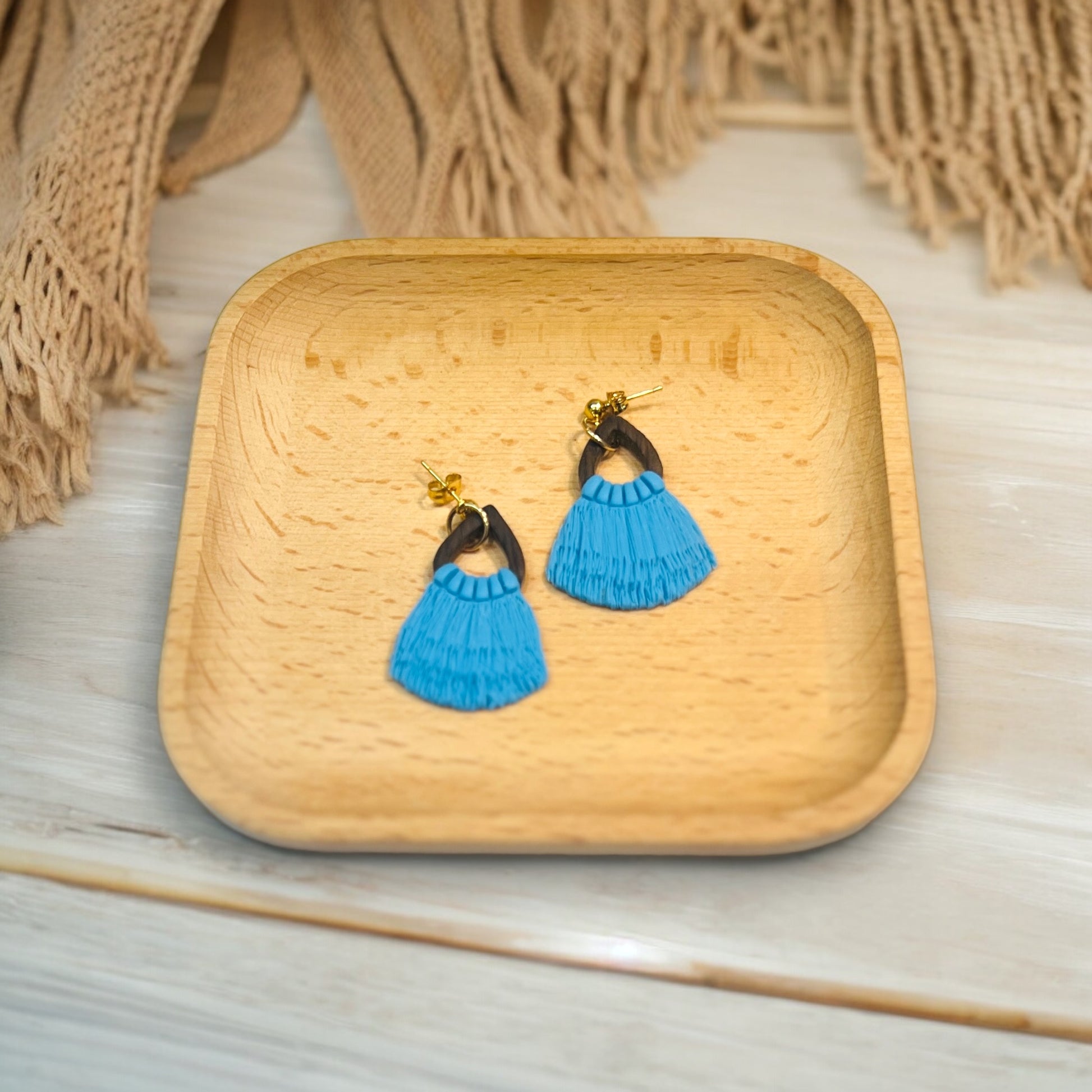 Handmade blue fringe drop earrings with a dark wood accent and gold hardware, placed in a wooden tray with a cozy textile backdrop.