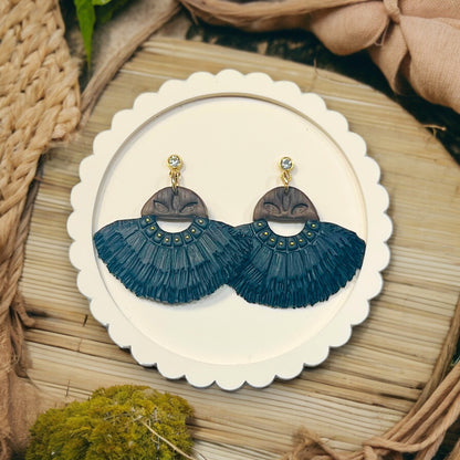 Black and wood-inspired fringe earrings featuring boho details with gold accents, displayed on a round textured plate. 