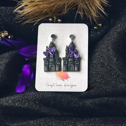 Gothic castle-themed earrings with purple bat accents displayed on a Craft Love Designs card, set against a dark, sparkly background.