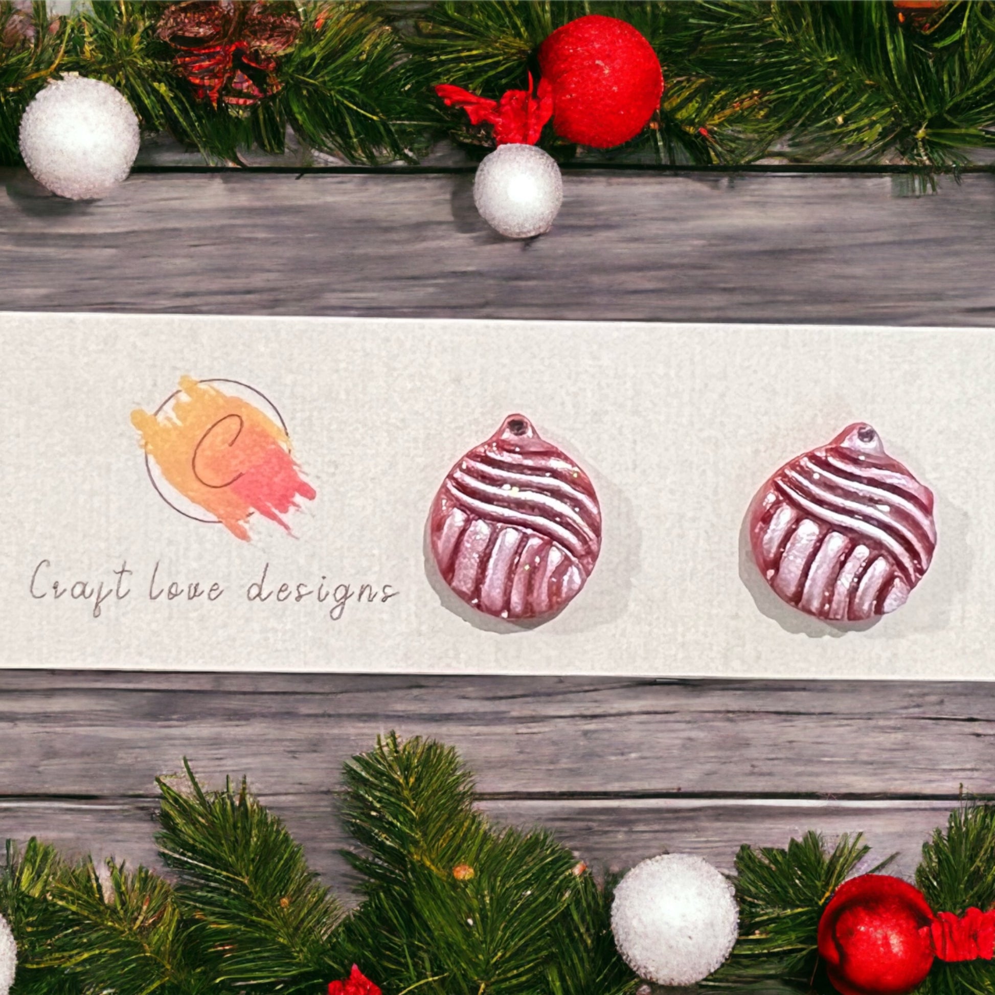 Frosty red ornament stud earrings with shimmery textures displayed on a festive backdrop, surrounded by Christmas greenery and decorations.