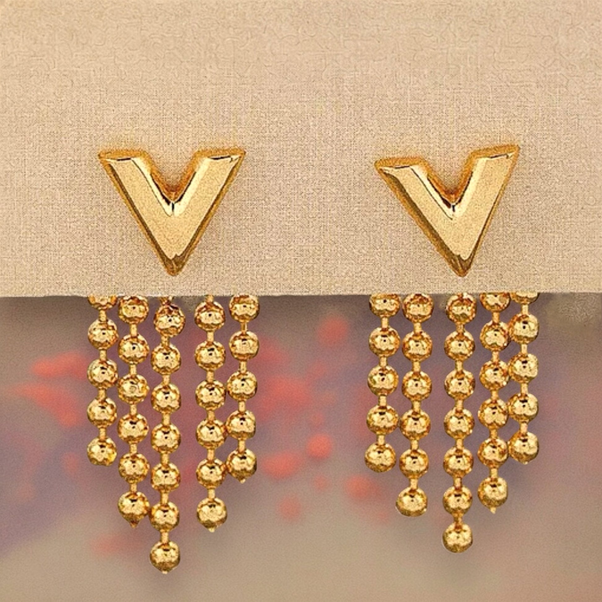  Close-up of gold V tassel earrings, showcasing bold V-shaped studs and cascading gold tassels for a stylish, modern finish.