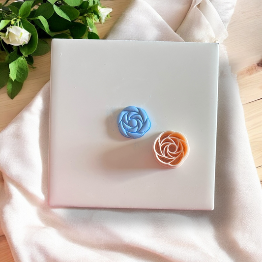 blue and peach rose-shaped polymer clay pieces on white tile with fabric