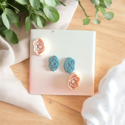 Pair of blue and pink earrings on a white card with green leaves in the background