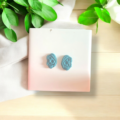 Pair of blue earrings on a pink card with green leaves in the background