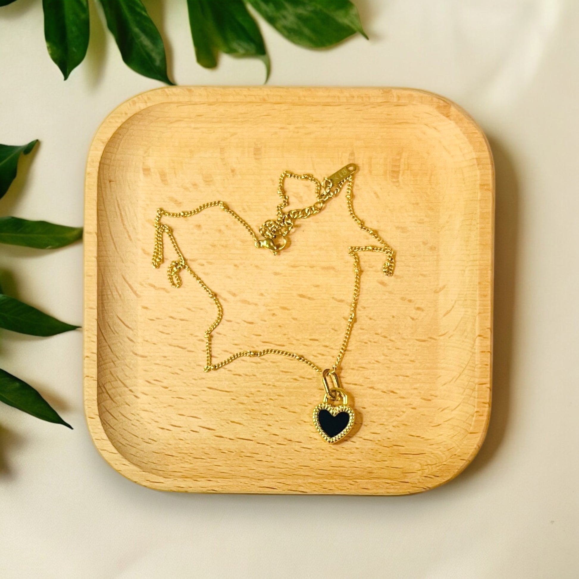 Double-sided gold heart pendant with black and white enamel, delicately placed on a wooden tray. 