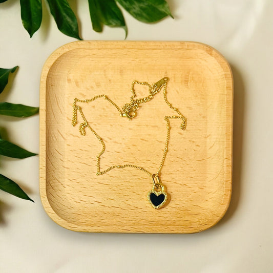 Double-sided gold heart pendant with black and white enamel, delicately placed on a wooden tray. 
