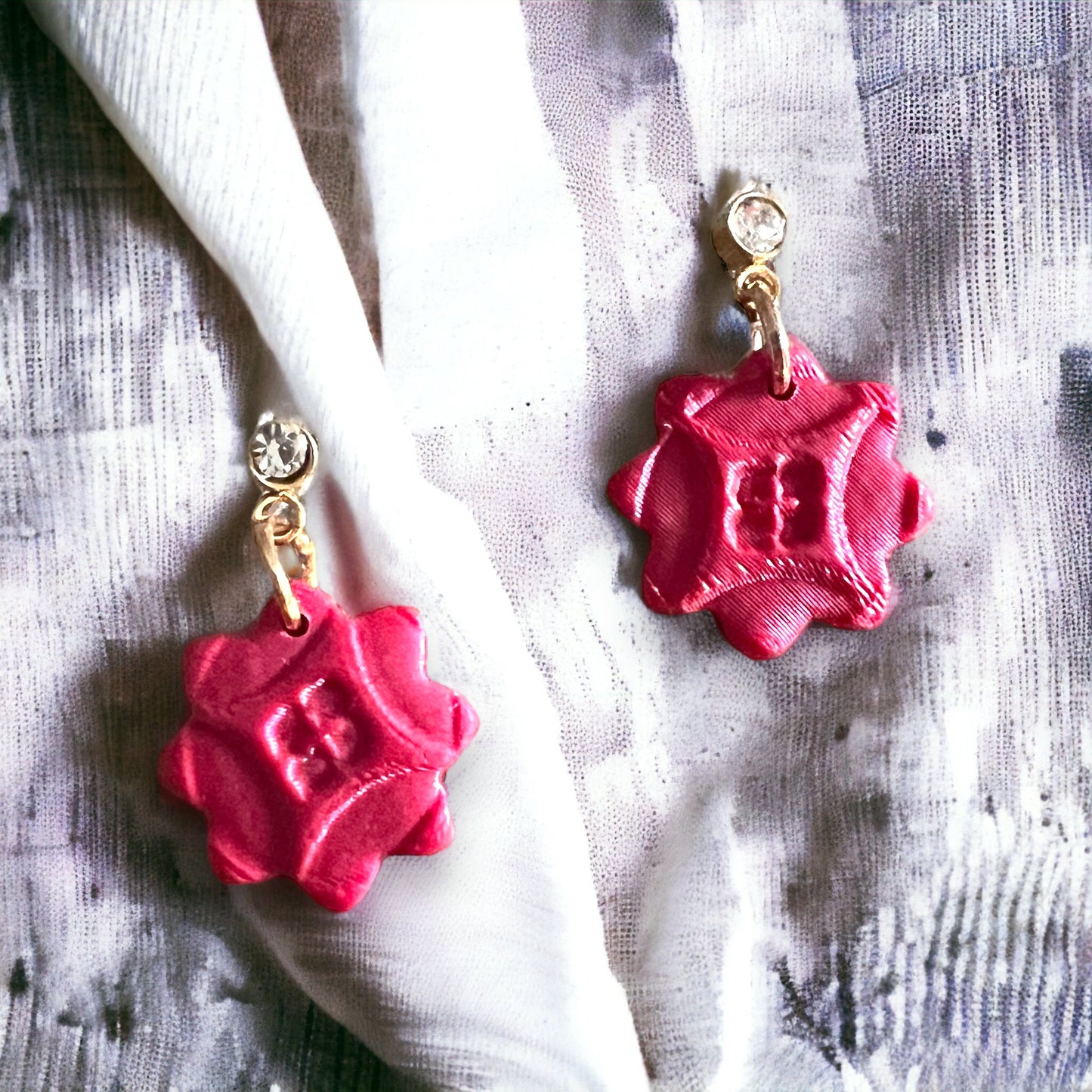 Red cubic zirconia dainty dangle earrings placed on a soft fabric, highlighting their intricate, petal-like design and elegant shine.
