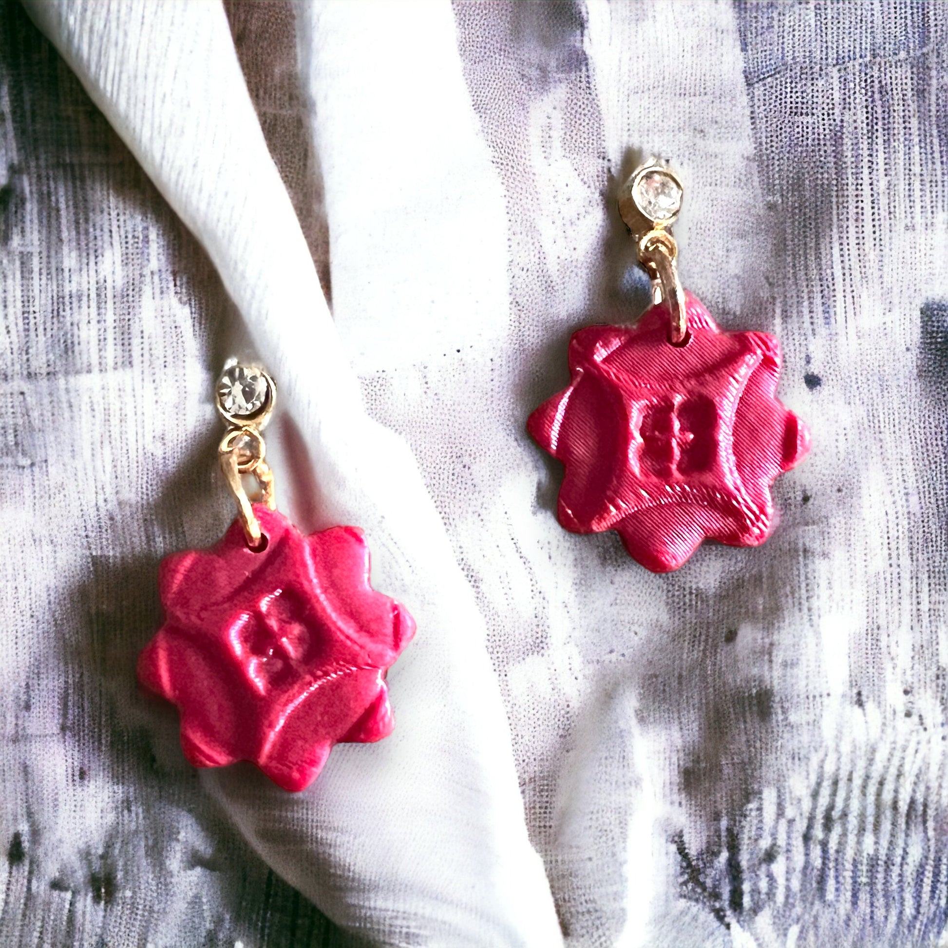 Red cubic zirconia dainty dangle earrings placed on a soft fabric, highlighting their intricate, petal-like design and elegant shine.

