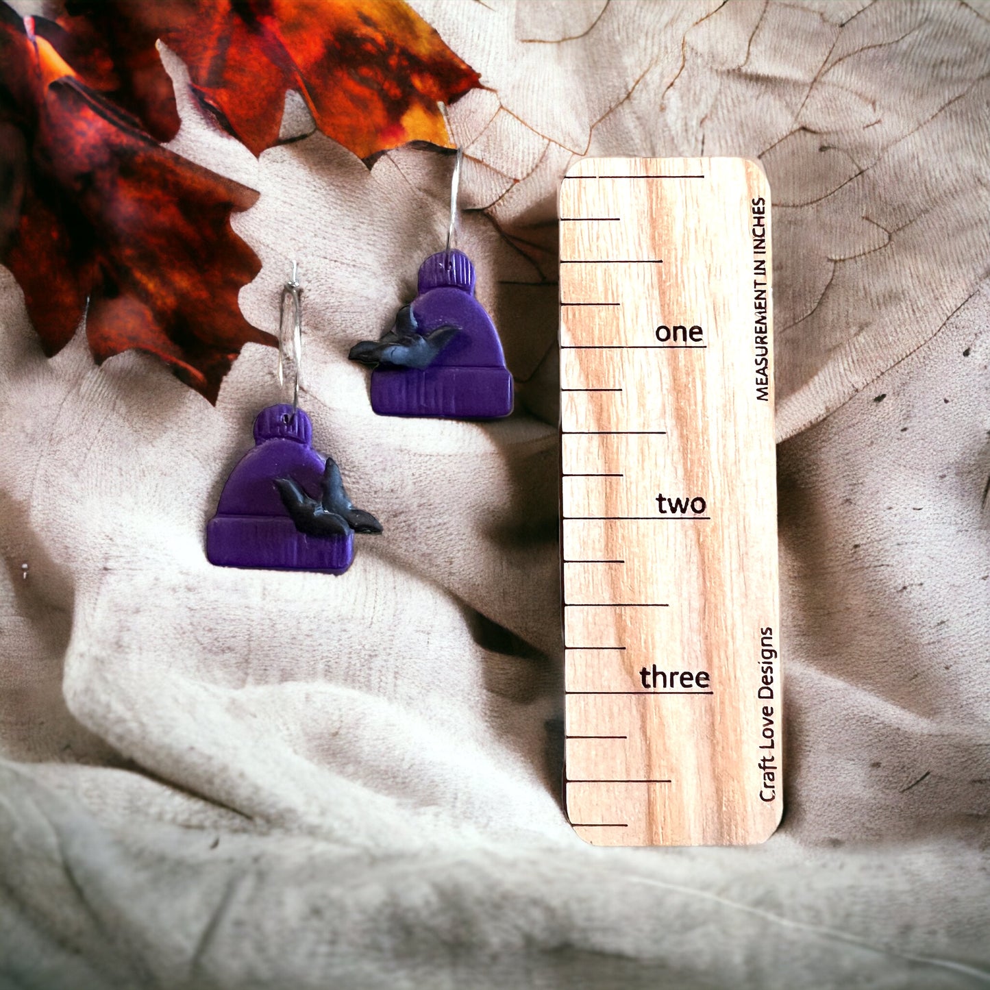 Purple polymer clay beanie earrings showcasing cute bat details. Autumn-themed dangle earrings with playful, cozy vibes.