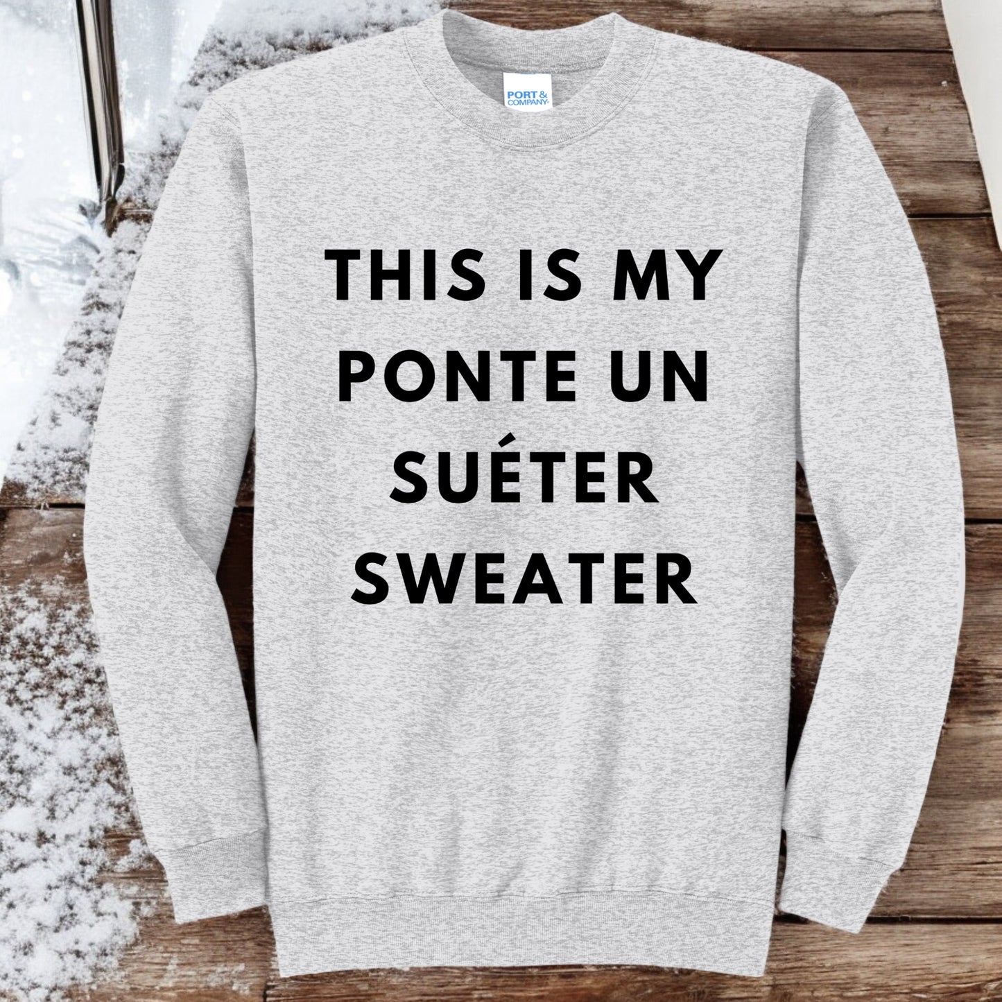 Flat lay of an ash gray crewneck sweatshirt with bold black text that reads "This Is My Ponte Un Suéter Sweater," displayed on a neutral background.