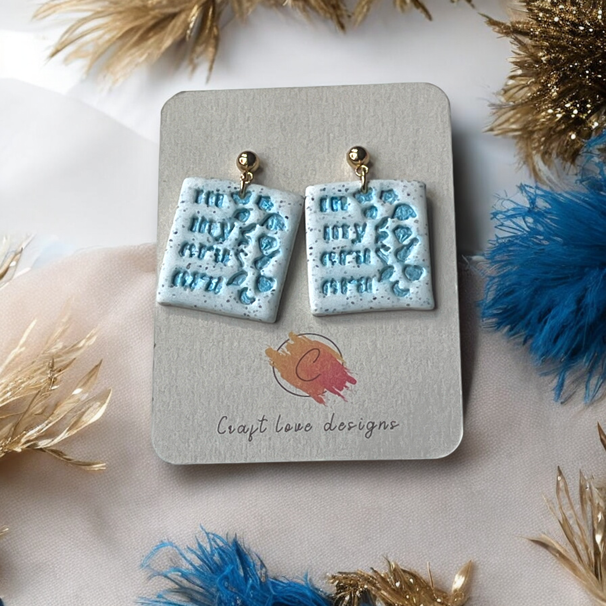 Fun and vibrant 'In My Eras Era' earrings displayed on a Craft Love Designs card, with light blue icons and sparkling details.