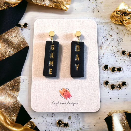 Black and gold polymer clay dangle earrings with "Game" and "Day" text, customizable design for sports enthusiasts.