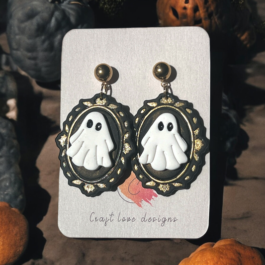 White ghost cameo earrings with ornate black and gold frames on a Craft Love Designs display card, surrounded by spooky decor. (