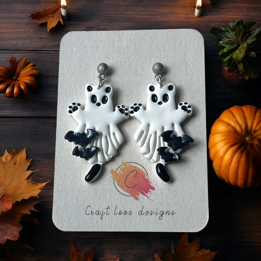 Playful white ghost earrings with paw prints and black bat accents displayed on a Craft Love Designs card, surrounded by autumn decor. 