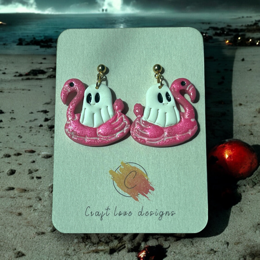 Cute handmade earrings featuring ghosts relaxing in pink flamingo floats, perfect for playful and spooky fashion enthusiasts.