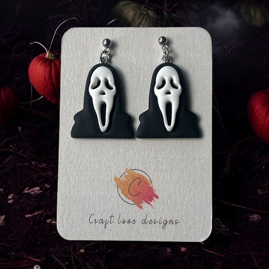 Ghostface-inspired horror earrings in black and white on a Craft Love Designs display card, set against a dark and eerie background